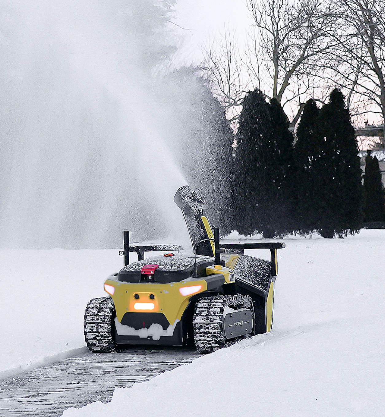 Yellow and black snow-clearing robot with glowing headlights ejects snow from its chute, clearing a path in a snowy yard with evergreen trees in the background.