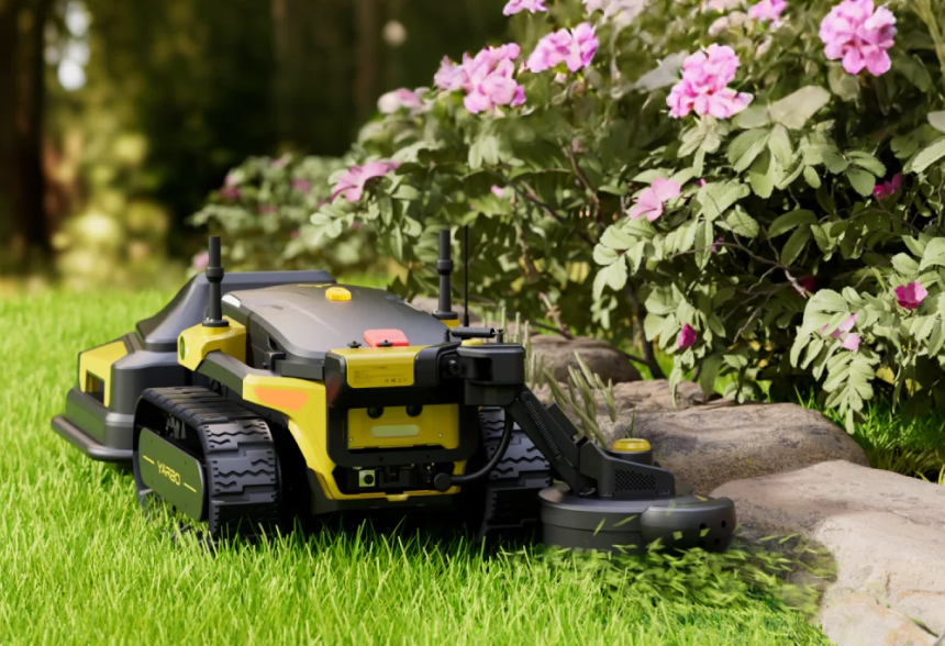 Yellow and black robotic lawn mower on green grass near pink flowers and rocks.