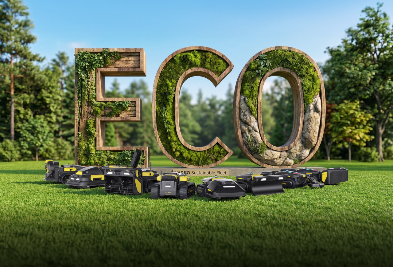 Large wooden "ECO" letters covered in moss and ivy stand in a grassy field, with black and yellow robotic lawn mowers lined up in front under a clear blue sky.