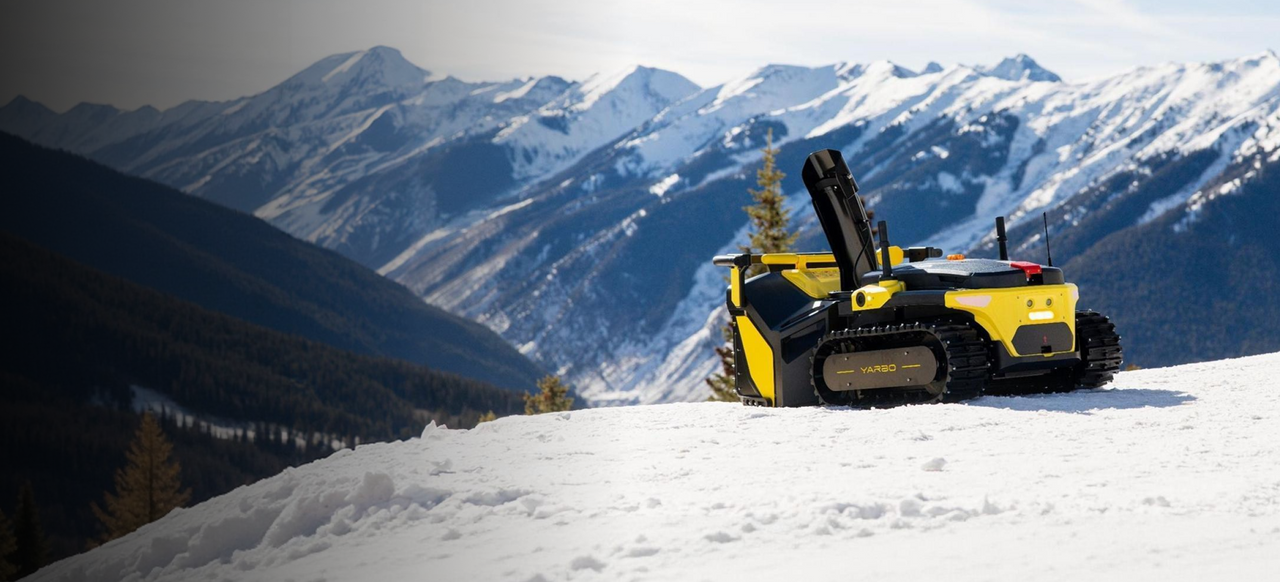 Yellow and black YARBO tracked robot on snowy slope with snow-capped mountains in background.