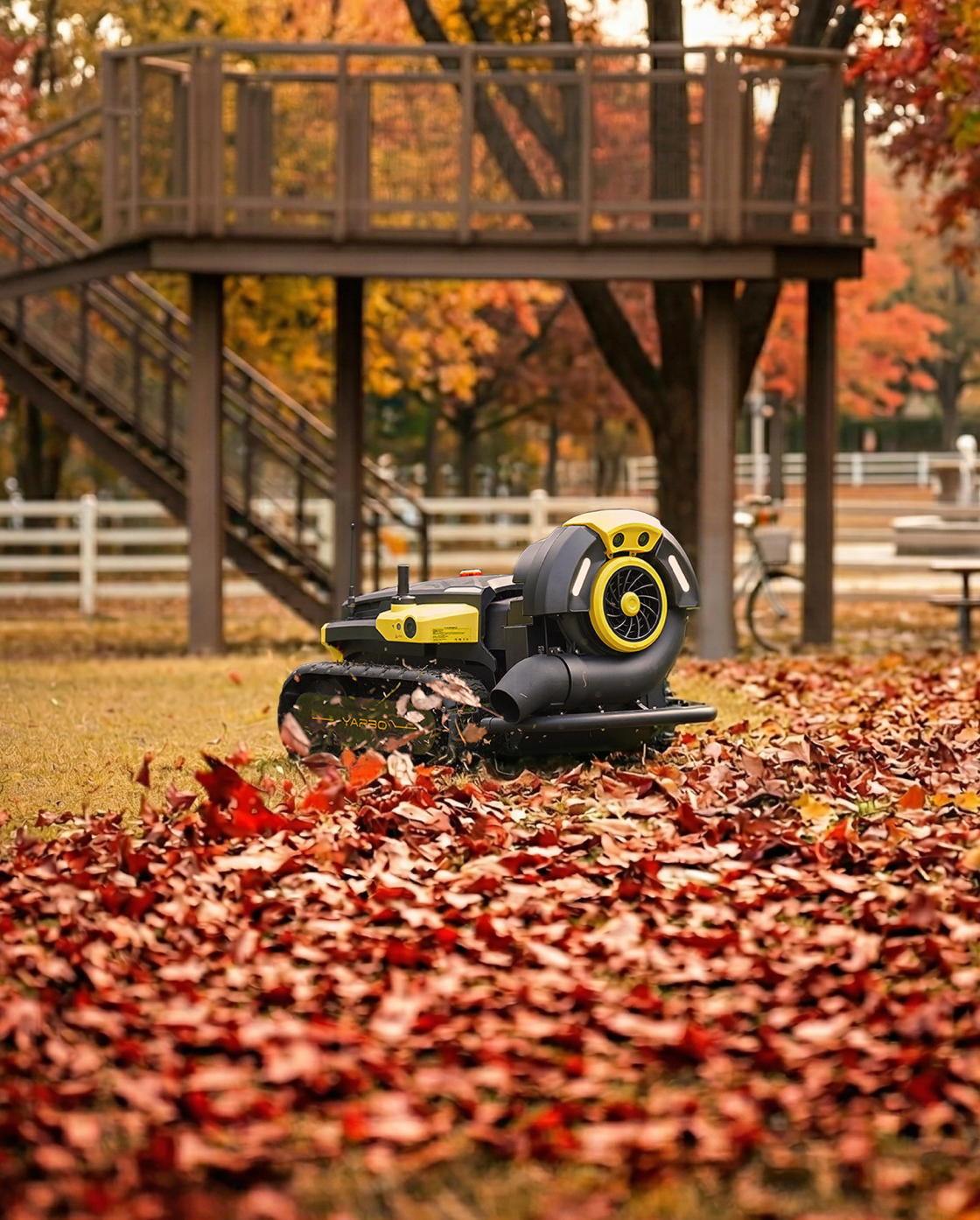Black and yellow robotic leaf blower by Yarbo with tracked base, blowing autumn leaves in a yard with wooden deck in background.