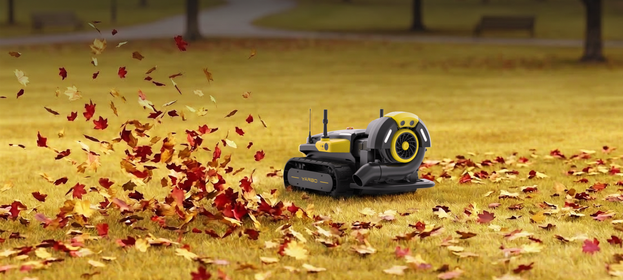 Yellow and black YARBO robotic leaf blower on grass, blowing red and orange autumn leaves in a park.
