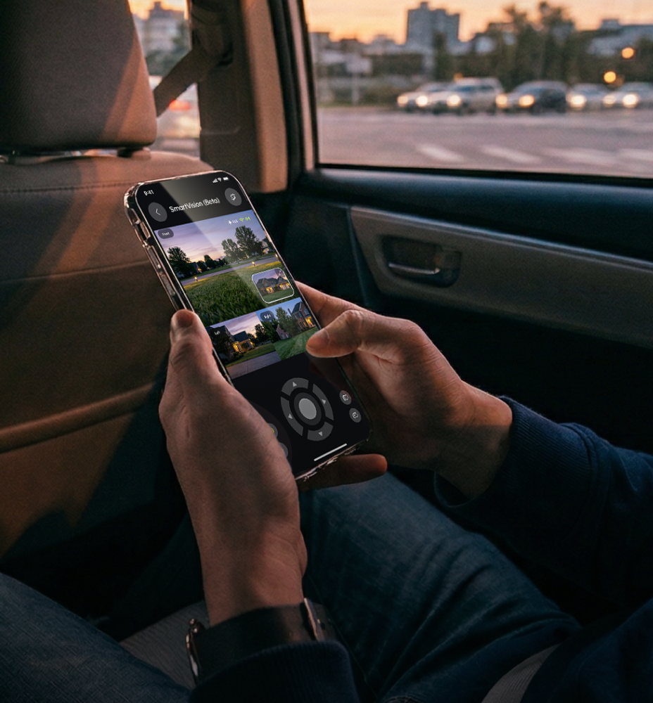 Hands holding smartphone with SmartVision app, showing home security camera feeds, inside car at dusk.