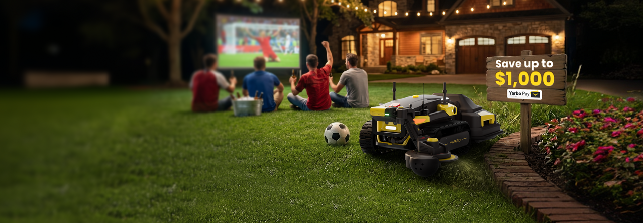 Yellow and black Yarbo robotic lawn mower on green grass, near soccer ball and wooden sign reading "Save up to $1,000" with "Yarbo Pay" logo, as men watch soccer on outdoor screen in background.