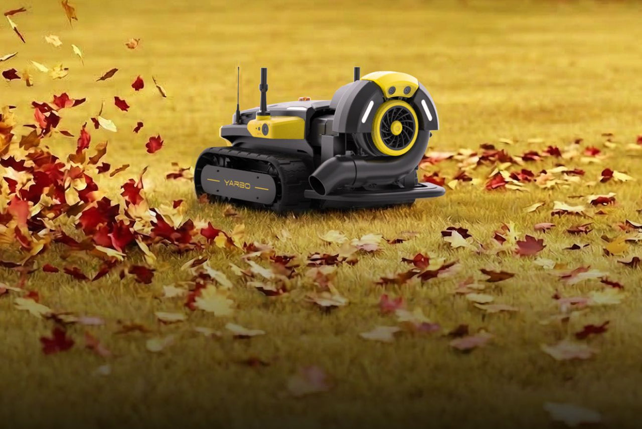 Yellow and black YARBO robotic leaf blower on grass, blowing red and orange autumn leaves.