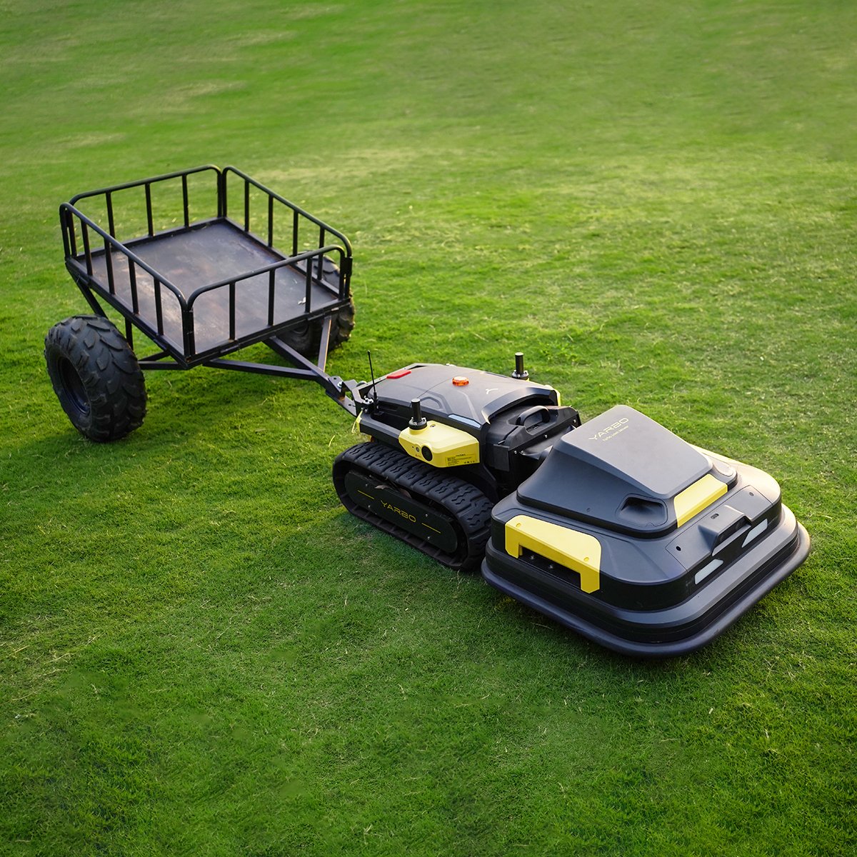 Black and yellow YARBO robotic lawn mower with attached utility cart on vibrant green grass.