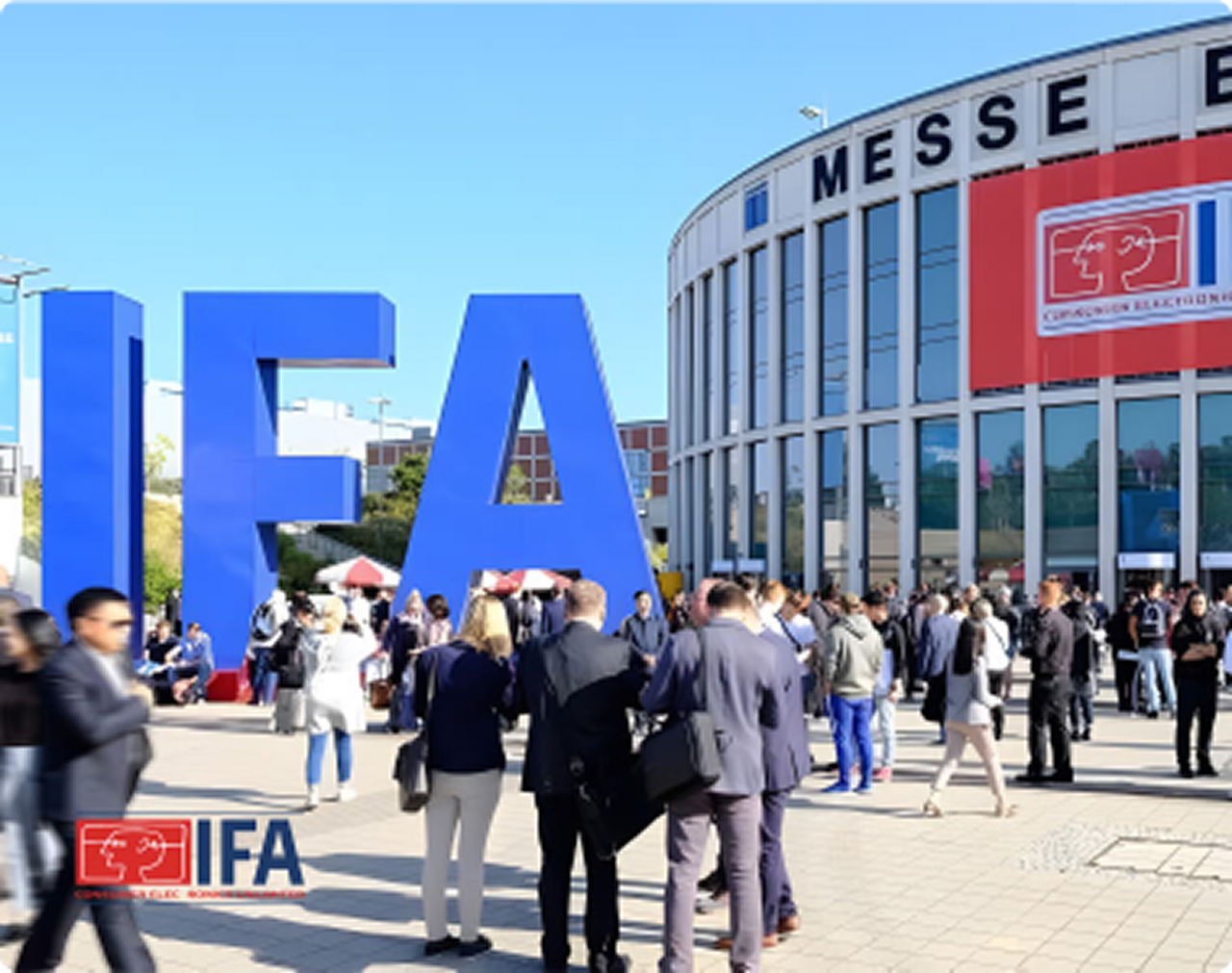 Large blue IFA letters in foreground, crowd gathering outside Messe Berlin building under clear blue sky.