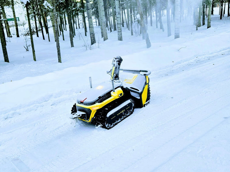 Yellow and black YARD robot on snowy path in winter forest, tracks visible, snow-covered trees in background.